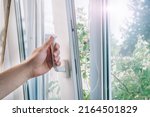 A man's hand holds a plastic window handle.Manual opening white plastic pvc window at home.A man opens a window, closes a plastic frame in his apartment.A man opens a window with a mosquito net.