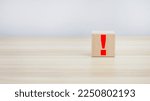 Small photo of Warning exclamation mark on a wooden block to attract attention over a grey background with beams of light and copy space