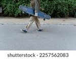 Woman holding her longboard while walking in a park.