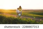 Small photo of mother rides child bicycle sunset. happy family park. Mom teaches her daughter ride bike. concept happy family summer park. fun vacation. teamwork. mother runs green grass rolling child bicycle.