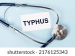 Small photo of Stethoscope and white card with TYPHUS text on blue background. Medical concept.