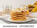 A stack of oatmeal banana pancakes with slices of fresh bananas, walnuts and honey on top with cup of tea on a white wooden background. A healthy breakfast. Copy space
