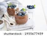 Chocolate chia pudding with blueberry, almonds and mint on top in a glass jar on a white wooden background. Healthy food. Copy space