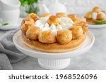 Saint Honore cake with profitrols, caramel, custard and whipped cream on a white plate on a gray concrete background. Traditional French dessert. Copy space