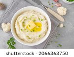 Cauliflower puree with butter and green onions in a white bowl on a gray concrete background. Healthy food. Copy space