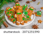 Gingerbread cookies in the form of man and christmas trees decorated with sugar glaze and sprinkled sugar candy on a plate on a gray concrete background. Pastries for Christmas and New Year