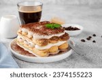 Tradition italian layered dessert tiramisu with mascarpone cream and biscuits on a white plate with cup of coffee on a gray concrete background