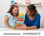 Two-year-old girl and her young kindergarten teacher, both Caucasian, play together in kindergarten, smiling happily