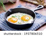 fried eggs with chives in an iron pan on a wooden table