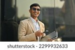 Cheerful asian businessman in photochromic glasses standing in front of modern office building outside