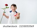 a boy of 4-5 years old holds a red rose and a gift in his hands. Cute baby, against the background of a white wall, horizontal photo