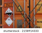 Small photo of Orange container lashed with lashing bars and twist locks on deck of container ship with stickers indicated dangerous goods inside. Class 6 is toxic and infectious and class 8 corrosive substances.