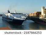 Small photo of Livorno, Italy - 07 31 2022: Ro-Ro, passenger ship with blue hull and white top operated by the Italian company Grimaldi Lines proceeding astern to berth position along fully loaded container vessel.