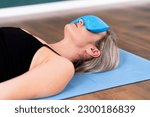 Small photo of Woman lying with blue silk aromatic pillow on eyes to deepen relaxation during Savasana practice female person relaxing body and mind on blue mat in yoga studio