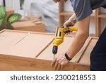 Small photo of Custom furniture assembling handyman fixing fasteners on wooden cabinet back side with professional screwdriver quality carpentry services specialist working with wood materials