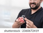 Small photo of Cheerful orthodontist putting transparent aligners on artificial lower jaw in modern stomatology clinic bearded dentist presenting device for teeth straightening