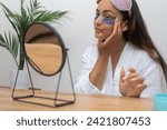 Small photo of Eyes Rejuvenated: A satisfied woman begins her day by applying under-eye patches to alleviate puffiness, wrinkles, and dark circles, gazing at her mirror reflection.