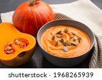 Small photo of Close up view of Hokkaido pumpkin cream soup in gray bowl toped with pumpkin seeds on gray background with copy space for text. Vegan food concept, homemade soup recipe. Selective focus