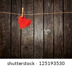 Red paper heart hanging on the clothesline. On old wood background.