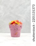 Small photo of Sop Buah or Es Campur in disposable plastic take away cup on grey background. Street fast food. Popular indonesian fruits cocktail dessert.
