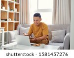 Young man is browsing at his laptop and calling with customer on the sofa at home, Business success