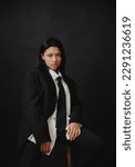 Small photo of A young African American woman sits on a chair in a business suit on a black background. A pretentious young black woman.