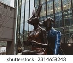 Small photo of Canary Wharf, London-23.01.23: Gillie Marc Tandem Lovers sculpture of Rabbitwoman and Dogman, illustrating scene in dark tones and low saturation standing in front of Reuters Plaza building.