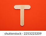Small photo of White wooden capital letter T on orange foamy background