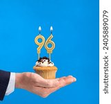 Small photo of Hand delivering birthday cupcake - Candle number 96 on blue background