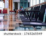 Framed composition shot of Asian man in airport, one person sitting alone at end of row of chairs, looking at his phone. Airport is empty. Selective focus.