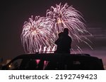 silhouette of a mother with her little daughter watching fireworks on the roof of their car