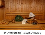 Wooden bucket with spoon, sauna hat, towels and broom on bench. Traditional finnish sauna interior detail and accessories