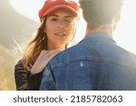 Small photo of Close-up portrait of beautiful young woman wearing cap with hand on boyfriend's shoulder enjoying sunset with him during weekend outing