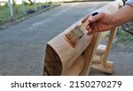 Small photo of varnishing a wooden bench at the initial stage in a rural yard, applying varnish protection to a solid wood product with a brush in a man's hand, finishing varnishing wooden furniture