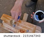 Small photo of varnishing a part of a wooden furniture structure by hand, hands holding a brush and a jar of varnish in the process of varnishing a wooden surface, applying varnish to solid wood furniture