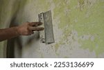 Small photo of scraping off unevenness and residues of paint and plaster with a spatula, cleaning and preparing the surface of a room wall before sticking wallpaper, a hand scrapes off a layer on a dilapidated wall