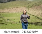 Small photo of young woman outdoors wearing an overcoat in the middle of green mountains