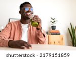 African American black man drinking healthy green juice with bamboo straw looking at camera. Copy space.