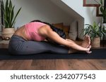 Young woman doing yoga stretching exercise, forward bend, paschimottanasana pose on mat at home.