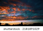 Small photo of Fiery evening sunset, orange-blue color. On the horizon are silhouettes of houses and trees. Landscape, cumbersome clouds.