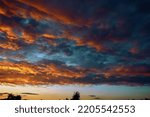 Small photo of Fiery evening sunset, orange-blue color. On the horizon are silhouettes of houses and trees. Landscape, cumbersome clouds.