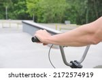 Small photo of athlete's hand on the handlebars of bmx bicycle in skate bmx park against the background of concrete figures