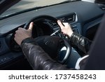 A young man in a black leather jacket sits behind the wheel of his car, on a Sunny day. Close-up of a man's hands on the steering wheel
