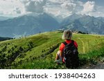 Blonde girl enjoying view during trekking in Alps, Austria.Majestic peaks of mountains,green meadows,view of valley. Active happy backpacker.Travel sport concept.Sitting relaxing female with backpack