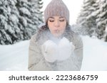 Young beautiful woman blowing snow off the hand.Winter outdoor activity, winter holidays.Selective focus, close up.