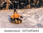 Small photo of Active toddler boy in a yellow jacket sliding down the hill on snow tube.Winter fun,active lifestyle concept.