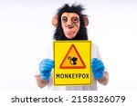 Small photo of Person dressed in a monkey mask, in a medical nurse's suit, holding a sign with the danger sign and a monkey, which reads: MONKEYPOX, on a white background. Virus, epidemic, Nigeria and smallpox.