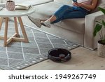 Robotic vacuum cleaner cleaning carpet, woman remote control mobile phone and enjoy rest, sitting on sofa at home