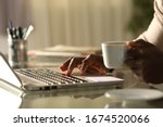 Close up of a black man hands using laptop holding a coffee cup in the night on a desk at home