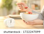 Close up of woman hands eating cereal bowl with fruit after intermittent fasting sitting on a table at home